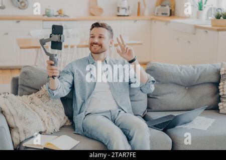 Ein Mann in lässiger Kleidung nimmt einen Video-Blog auf, gibt ein Friedenszeichen mit Telefon und Gimbal. Stockfoto