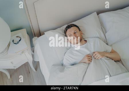 Mann, der im Bett liegt und nicht schlafen kann, angespannt und besinnlich aussieht, Schlaflosigkeit-Konzept. Stockfoto