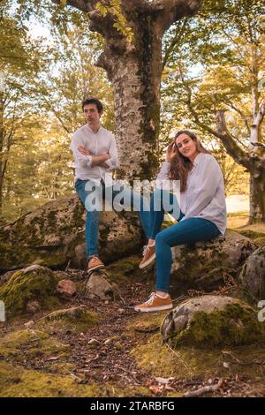 Vertikales Porträt eines lässigen Paares in Denim-Kleidung, das auf einem Wald sitzt Stockfoto