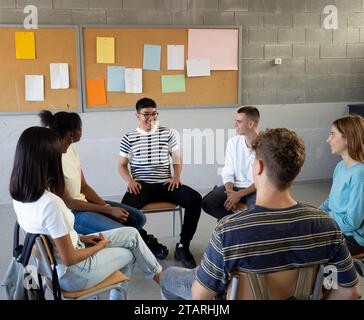 Gruppe von verschiedenen Teenagerstudenten, die miteinander sprechen und in einem Kreis sitzen, in einem Klassenzimmer einer Schule Stockfoto