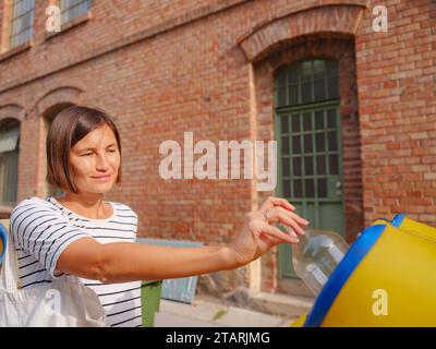 Eine Frau, die Plastikbehälter auf der europäischen Straße wirft. Abfalltrennung Müll, bevor er in den Abfalleimer fällt, um Welt und Umwelt zu retten. Konzept für die Abfallverwertung Stockfoto