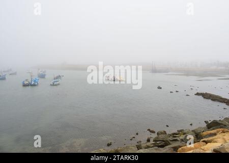 Unbearbeitetes Foto von Fischerbooten in einem Hafen bei nebeligem Wetter Stockfoto