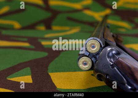 Geöffnetes Jagdgewehr mit Patronen auf einem Tarnhintergrund mit Kopierraum für Text. Selektiver Fokus. Stockfoto