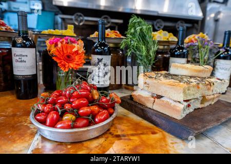 Argentinien, Buenos Aires, San Telmo Market. Lokales italienisches Café, Kräuterfladenbrot, roma Tomotoes mit Weinflaschen in der Ferne. Stockfoto