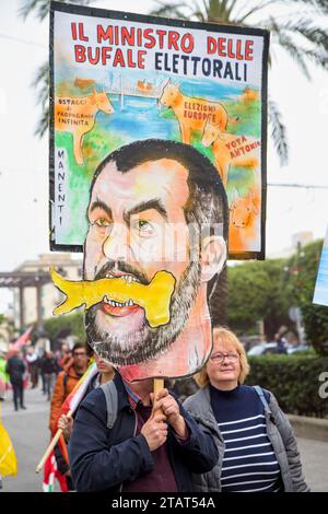 Messina, Italien. Dezember 2023. Ein Mann versteckt sich hinter einem Schild mit der Karikatur von Matteo Salvini, dem Minister für Infrastruktur, und den Worten "Minister der Wahlhoaxes" während des Protests gegen den Bau der Strait Bridge, organisiert von der No Bridge Coordination in Messina. Etwa zweitausend Menschen protestierten gegen den Bau der Brücke über die Meerenge von Messina, der längsten Hängebrücke der Welt in einem Gebiet, das heftigen Winden und starken Gezeitenströmen ausgesetzt ist, in einem der Gebiete mit dem höchsten Erdbebenrisiko im Mittelmeer. Hunderttausende von Quadraten Stockfoto