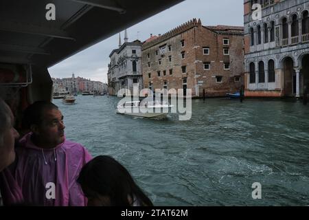 Venedig im Regen; Touristen schauen aus einem überfüllten ACTV No. 1 Vaporetto auf den palazzo, während er an einem regnerischen Tag den Canal Grande entlang fährt. Stockfoto