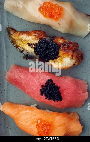 Verschiedene Nigiri-Sushi auf einem Teller, auf dunklem Beton Stockfoto