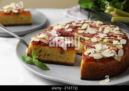 Frisch gebackener Rhabarberkuchen mit Mandelflocken und Tortenheber auf weißem Tisch, Nahaufnahme Stockfoto