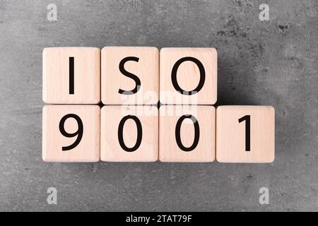 Holzwürfel mit Abkürzung ISO und Nummer 9001 auf grauem, strukturiertem Tisch, flach liegend Stockfoto