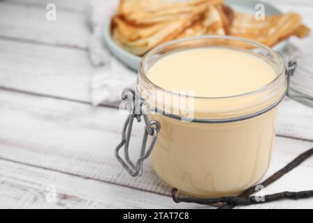 Leckere Kondensmilch im Glas, Crepes und Vanilleschoten auf weißem Holztisch, Nahaufnahme. Leerzeichen für Text Stockfoto