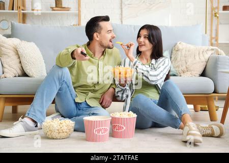 Ein junges Paar mit Kartoffelchips und Popcorn, das zu Hause fernsieht Stockfoto