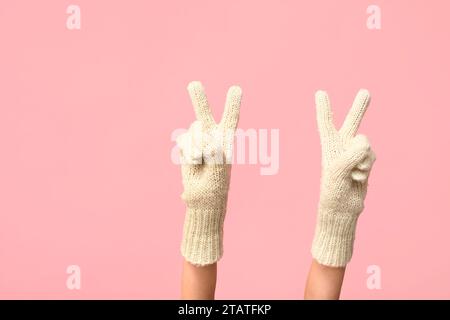 Hände in warmen Handschuhen mit Siegesgesten auf rosafarbenem Hintergrund Stockfoto