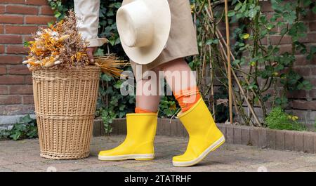 In gelben Stiefeln stehen hinter dem Korbkorb im Herbstgarten Stockfoto