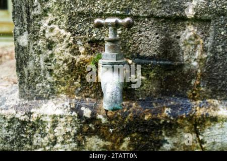 An einem alten Wasserbehälter ist ein Tropfhahn angebracht. Ein Wassertropfen wurde beim Herunterfallen aufgefangen. Stockfoto