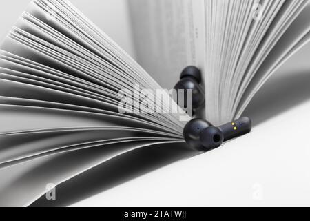 Kabellose Kopfhörer liegen auf der Mittelfalte eines Buches. Hören von Hörbüchern. Stockfoto