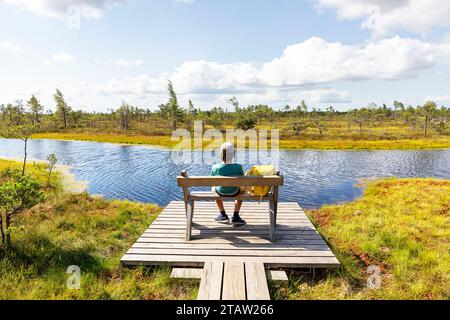 Touristen sitzen auf einer Bank in einem Kemeri Nationalpark an einem Sommertag, umgeben von Moos, Kiefern, Pools, winzigen dunklen Seen, Lettland Stockfoto