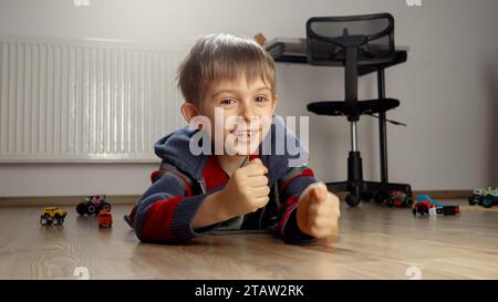 Fröhlich lächelnder Junge, der auf dem Boden lag und nach dem Spielen jubelte. Stockfoto