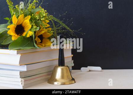 Sonnenblumenstrauß, Bücher und Glocke auf dem Hintergrund der Tafel, Konzept zurück zur Schule und Teacher Day Stockfoto