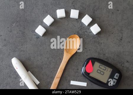 Zuckerwürfel mit Löffel für hohen Zuckergehalt, roter Bluttropfen und Glucometer, Diabeteskonzept Stockfoto