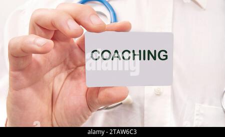 COACHING-Wort auf der Karte in der Hand eines Mannes auf dem Hintergrund eines weißen Hemdes Stockfoto