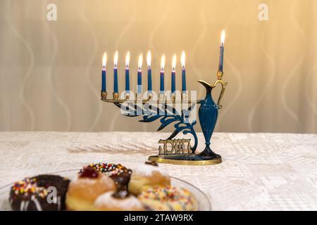 Menora mit brennenden Kerzen für jüdischen Hanukka-Urlaub auf dem Tisch zu Hause. Wir feiern das Chanukah-Lichterfest. Sufganiyot und Donuts. Stockfoto