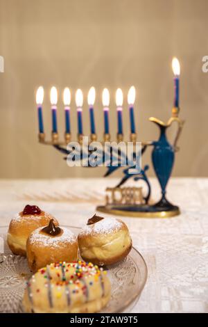 Menora mit brennenden Kerzen für jüdischen Hanukka-Urlaub auf dem Tisch zu Hause. Wir feiern das Chanukah-Lichterfest. Sufganiyot und Donuts. Stockfoto