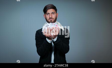 Junger Mann, der Karten vor grauem Hintergrund hält, Fokus auf Karten, Spielkarten Stockfoto