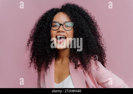 Überschwängliche junge Frau in Brille und rosa Blazer lacht fröhlich. Stockfoto