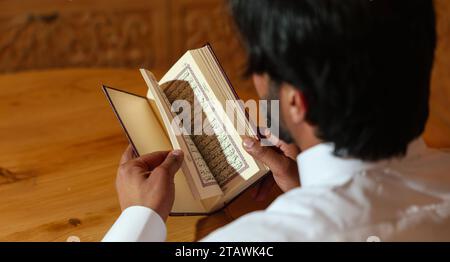 Muslimischer Mann, der den heiligen Koran liest. Der heilige Quran in der Hand mit arabischem Text, was Al Quran bedeutet. Stockfoto