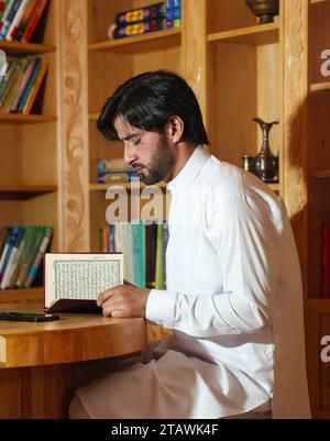 Muslimischer Mann, der den heiligen Koran liest. Der heilige Quran in der Hand mit arabischem Text, was Al Quran bedeutet. Stockfoto
