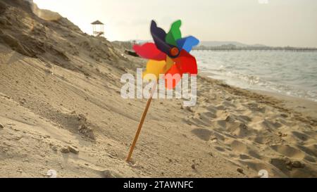 Ein farbenfrohes Windrad dreht sich in der Brise an einem Sandstrand, sorgloser Geist des Reisens, der Urlaubszeit und der Suche nach Glück Stockfoto