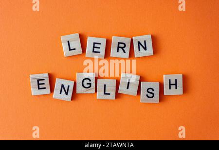 Word Englisch lernen. Motivation. Der Satz ist in Holzbuchstaben von oben angeordnet. Motivation. Orangefarbener flacher Lay-Hintergrund Stockfoto