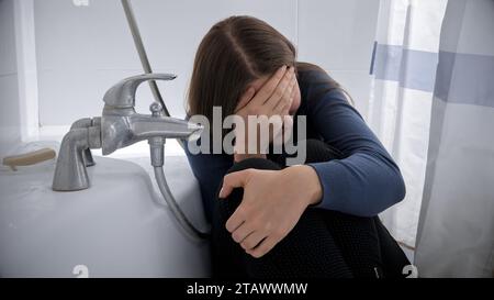 Verärgerte, weinende Frau, die im Bad sitzt, nachdem sie Opfer von Missbrauch oder Gewalt wurde. Stockfoto