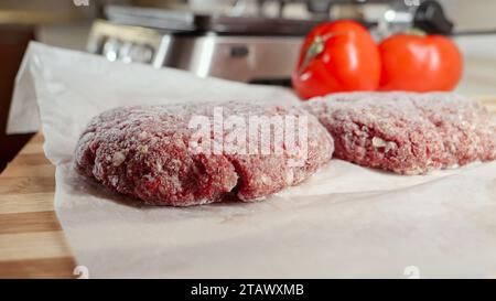Gefrorene Hamburger-Pasteten und Zutaten liegen auf dem Küchentisch neben dem elektrischen Grill Stockfoto