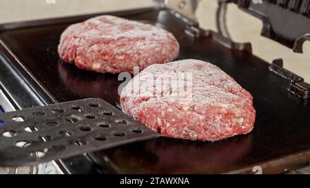 Nahaufnahme von Hand, die gefrorene Hamburger-Rindfleisch-Patties auf heißen Grill gelegt hat. Kochen zu Hause, Küchengerät, gesunde Ernährung, Hamburger Zutaten Stockfoto