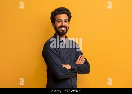 Selbstbewusster junger indischer Mann, der Arme über gelbem Hintergrund gekreuzt hat Stockfoto