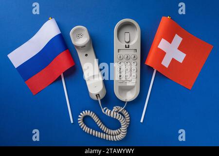 Altes Telefon und zwei Flaggen auf blauem Hintergrund, Konzept zum Thema Telefongespräche zwischen der Schweiz und Russland Stockfoto