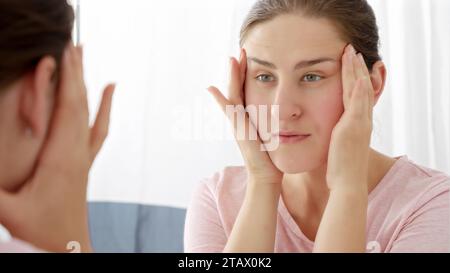 Porträt einer jungen besorgten Frau, die Haut unter die Augen zieht, um Alterungsfalten zu entfernen. Stockfoto