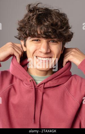 Fröhlicher junger Erwachsener in einem rosafarbenen Hoodie mit fröhlichem Ausdruck vor einem dezenten urbanen Hintergrund Stockfoto