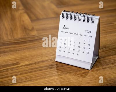 Ein Februar 2024 auf dem Kalender-Schreibtisch für den Organisator, um auf Holzhintergrund mit Platz und minimalem Stil zu planen und zu erinnern. Weißer kleiner Tischkalender mit Stockfoto