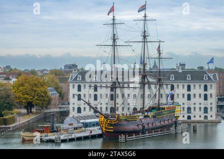 Niederlande. Bewölkter Sommertag in Amsterdam. Mittelalterliches Dreimasten-Segelschiff und das Gebäude des Maritimen Museums Stockfoto