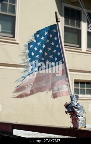 Eine zerrissene und zerrissene, verwitterte, alte amerikanische Flagge, die auf dem Dach eines Autos befestigt ist, flattert im Wind Stockfoto