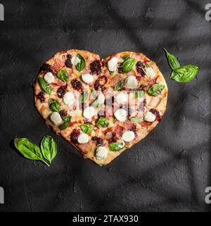 Köstliche und knusprige rote Frucht-Pizza in Herzform mit Basilikum Stockfoto