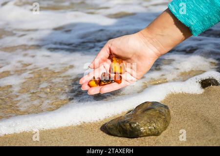 Schöne Stücke von Bernstein in der Hand des Meeres Hintergrund. Ein leuchtendes, welliges Stück Bernstein in der Handfläche. Der Sonnenstein Stockfoto