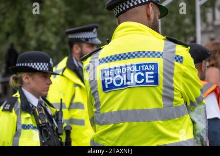 Metropolitan Police Schild auf der Rückseite einer gut sichtbaren Jacke, getragen von Polizisten, die eine Demonstration auf der Straße durch London überwachen. Stockfoto