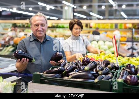 Ein reifer Käufer wählt reife Auberginen im Lebensmittelgeschäft Stockfoto