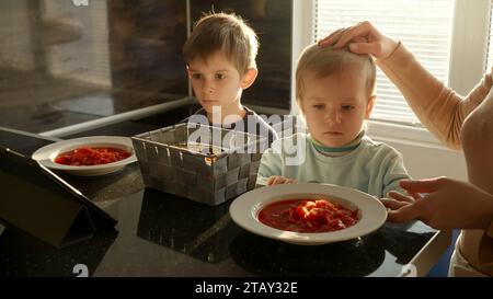 Junge Mutter, die Suppe für ihre Kinder auf den Esstisch stellt. Häusliches Essen, Kochen zu Hause, Kinder gesunde Ernährung Stockfoto