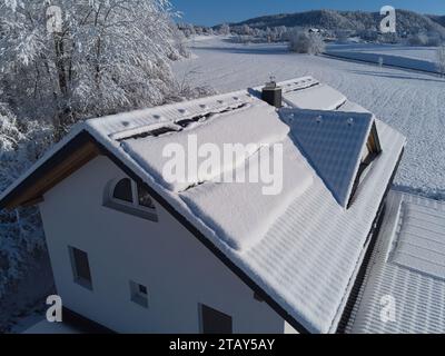 Schneebesen decken Solarpaneele auf einem Hausdach im Winter. Trotz der kühlen Umgebung sind die Photovoltaik-Panels widerstandsfähig. Perfekt für Illustratoren Stockfoto