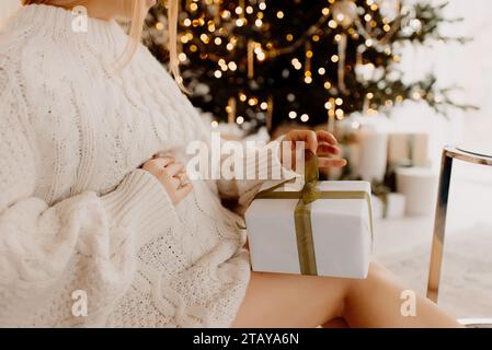 Blonde schwangere Frau, die sanft ihren Bauch vor dem Hintergrund des weihnachtsbaums berührt Stockfoto