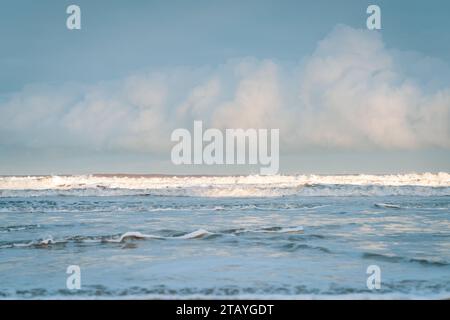 Beobachten Sie die weißen Wellen am Longsands Beach Tynemouth mit Surfern, die an einem eisigen Wintertag mit Schnee am Strand und hellblauem Himmel Wellen fangen. Stockfoto